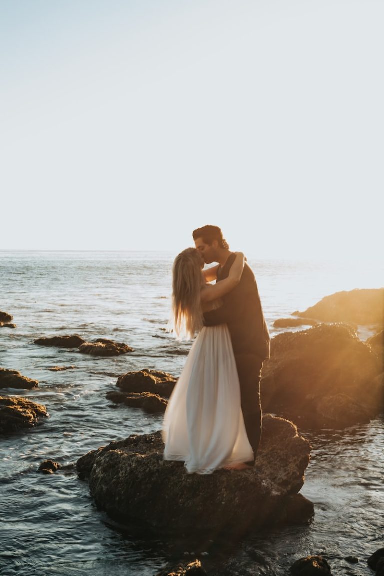 man and woman kissing on top of gray rock at beach